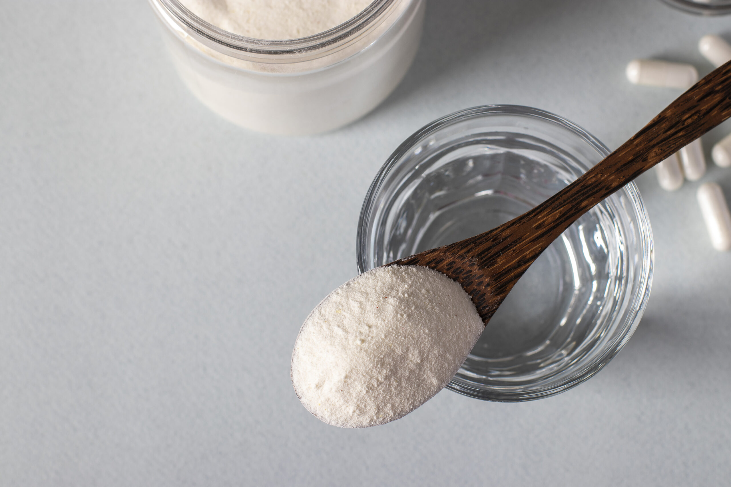 Collagen powder in spoon on glass of water, collagen capsules on light background, healthy and antiage concept View from above